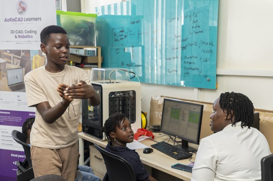 Young learners coding on screen beside a 3D printer